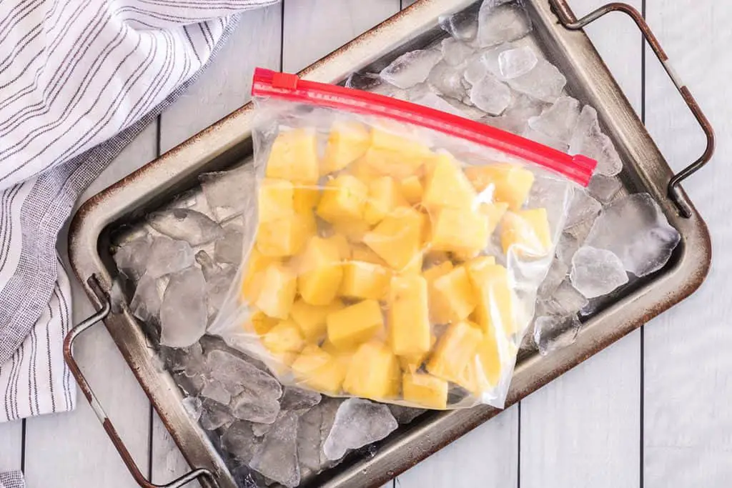 Frozen pineapple chunks in a zip lock bag sitting on top of a tray of ice showing how to freeze pineapple.