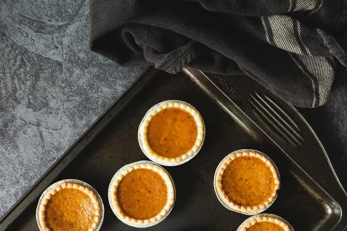 mini pumpkin pies sit on a sheet pan getting ready to go back into the oven after being frozen then thawed.