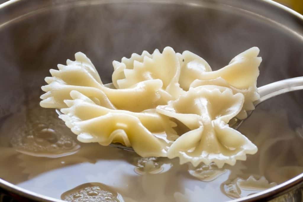 bow tie pasta being scoped out of boiling water after being reheated from being frozen.