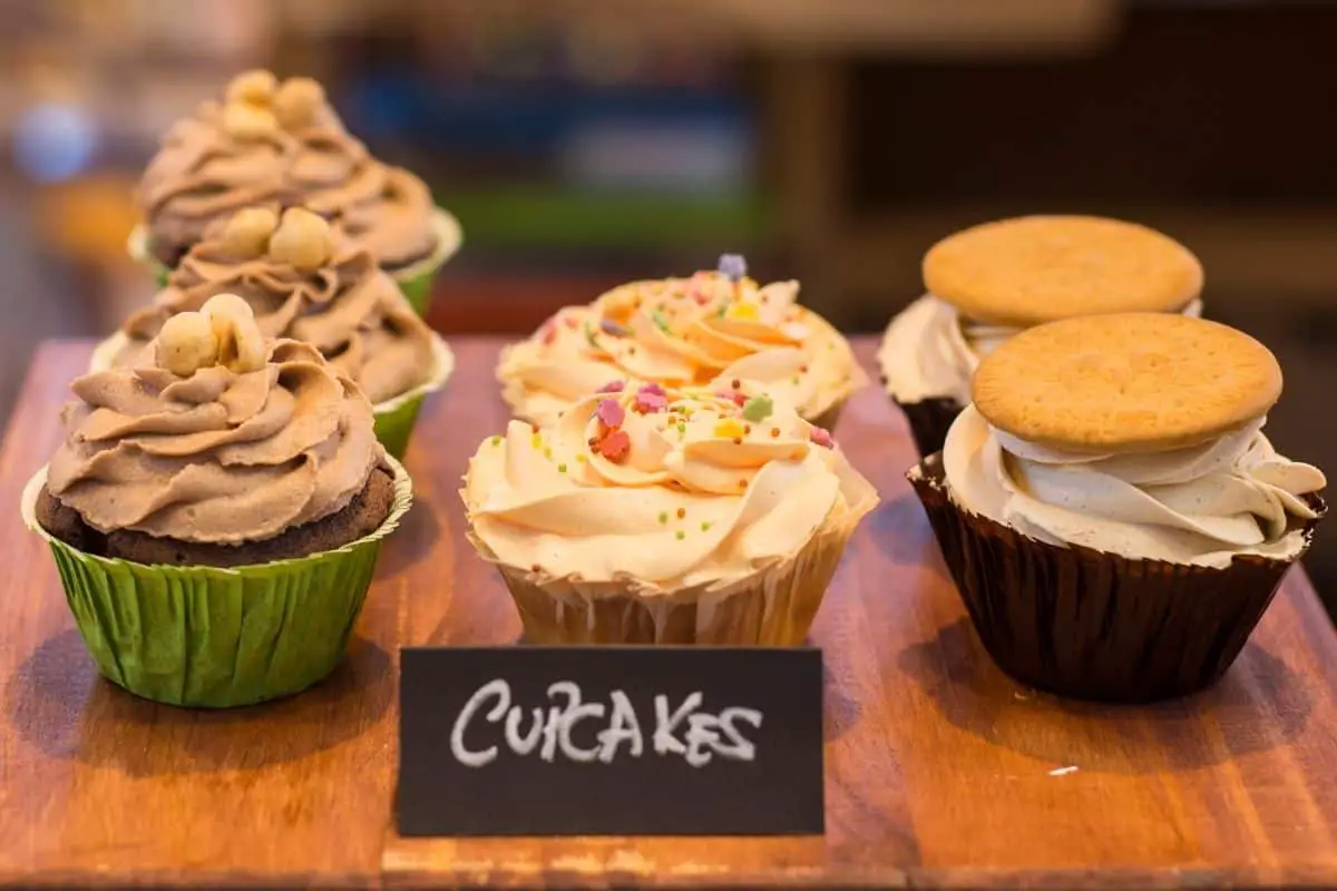 three rows of different flavor cupcakes are on display with a sign that says cupcakes in front of it representing how to price cupcakes