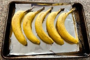 a row of bananas on a sheet pan getting ready to be ripened in the oven for use in banana bread