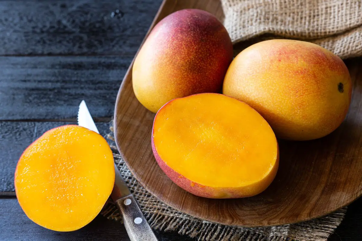 how to tell if a mango is ripe with two whole ripe mangoes and one ripe mango cut in half with ripe flesh