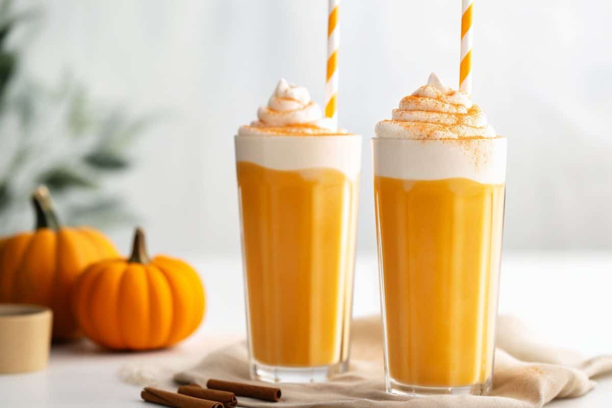 two glasses of a pumpkin smoothie with whipped cream on top with pumpkin pie spice